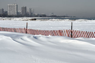 Snow covered land with snowdrifts and snow fence against sky