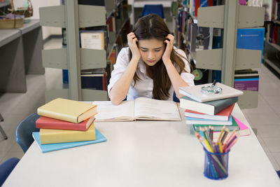 Tensed female student studying at table in library