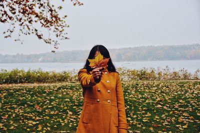 Woman holding maple leaf while standing on field during autumn