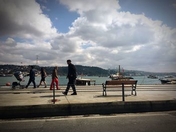 People walking on pedestrian walkway against cloudy sky