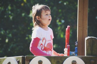 Cute girl standing at outdoor play equipment against trees