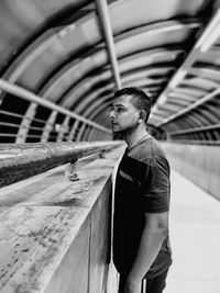 Side view of young man looking away while standing by railing on bridge