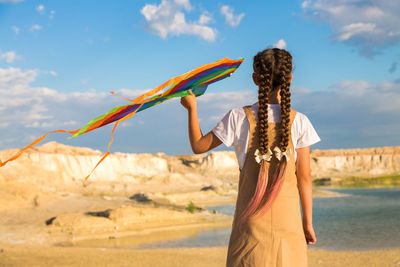 Rear view of woman standing at beach against sky