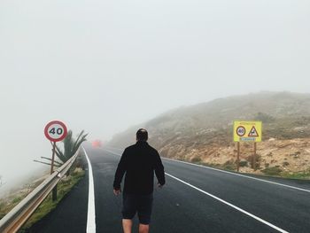 Rear view of man walking on road against sky during foggy weather