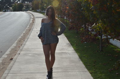 Full length portrait of young woman standing on sidewalk by trees