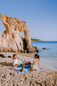 Girl sitting on beach by sea against clear sky