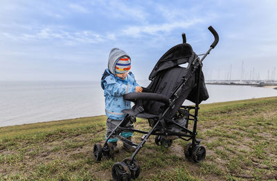 Toddler standing by stroller on field against sky