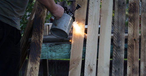 Midsection of man burning wooden plank outdoors