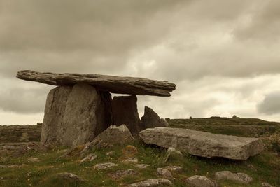 View of rock on field against cloudy sky