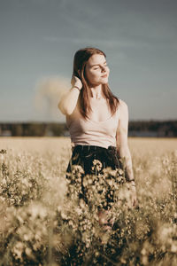 Young woman standing on field against sky