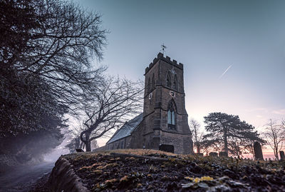 Low angle view of tower amidst trees and buildings against sky