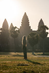 Rear view of woman standing on field against sky during sunset