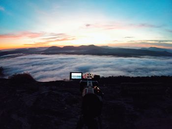 Rear view of man photographing against sky during sunset