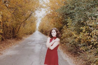 Portrait of young woman in red dress standing on road in forest