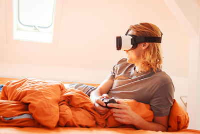 Young woman using mobile phone while sitting on bed at home