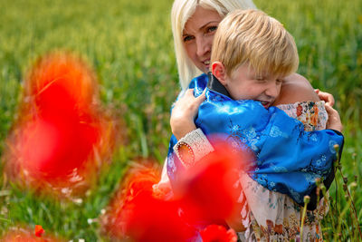 Mother embracing son by plants on field