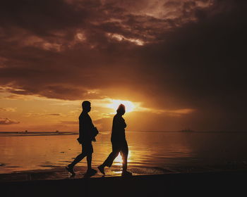 Silhouette men standing on beach against sky during sunset