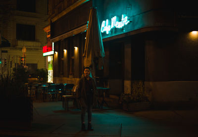 Rear view of man walking on illuminated street at night