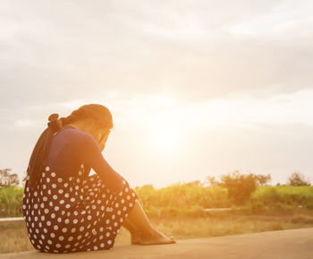 Rear view of woman sitting on land against sky during sunset