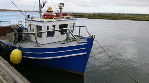 Fishing boat moored on pier by sea against sky