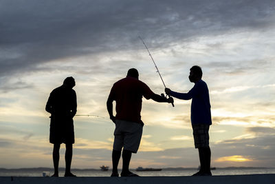 Silhouette people standing on land against sky during sunset