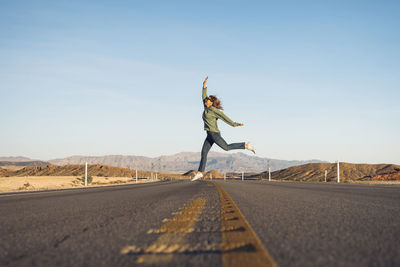 Woman jumping on road against sky