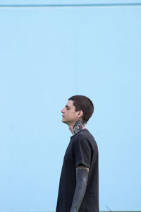 Side view of young man looking away against blue wall