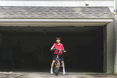 Portrait of boy with bicycle standing at garage