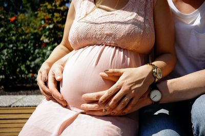 Midsection of pregnant woman with man sitting outdoors