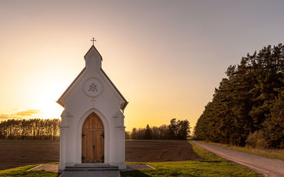 Cross amidst trees and buildings against sky during sunset