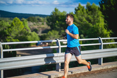 Young man jogging on by railing against sky