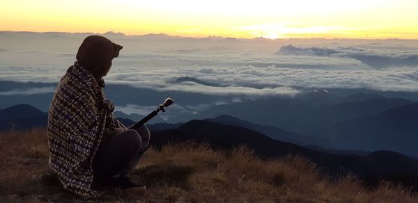 Man sitting on mountain against sky during sunrise