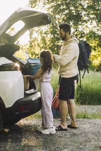 Side view of daughter and father unloading luggage from car trunk