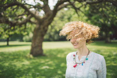 Smiling blond mid adult woman with tousled hair in park