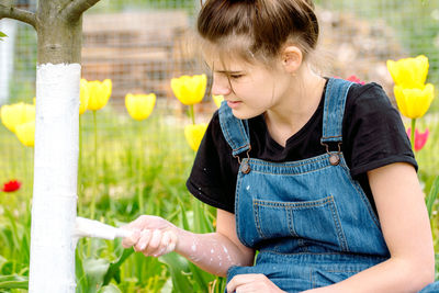 Teenager girl painting tree trunk outdoors