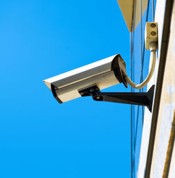 Low angle view of security camera against clear blue sky
