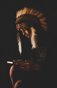 Woman wearing headdress holding book against black background