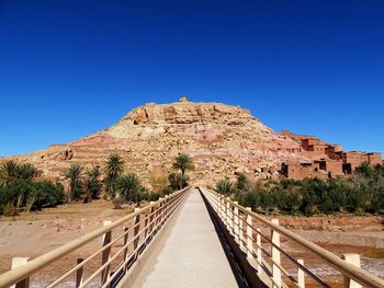 Walkway leading towards mountain against clear blue sky