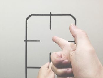 Cropped image of hand amidst metal pointing towards wall