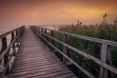 Boardwalk amidst field against sky during sunset