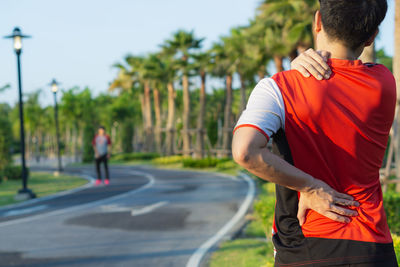 Rear view of man standing on road against trees