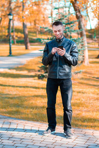 Portrait of young man standing on footpath during autumn