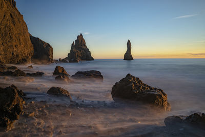 Rocks on beach against sky during sunset