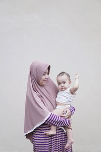 Mother carrying daughter while standing against wall