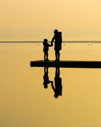 Mother standing with son by lake during sunset