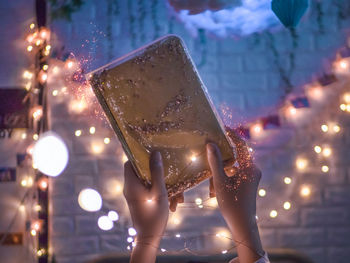 Digital composite image of woman holding illuminated christmas lights at night