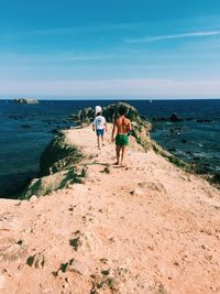 Rear view of shirtless man with friends on rock formation at beach against sky