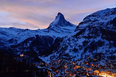 Illuminated residential district by snow covered mountains against sky