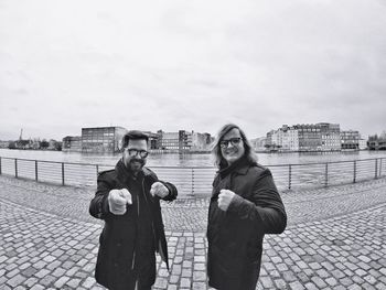 Portrait of male happy friends gesturing while standing on promenade against sky