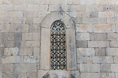 Large window with carved iron bars in the old brick building of light stone